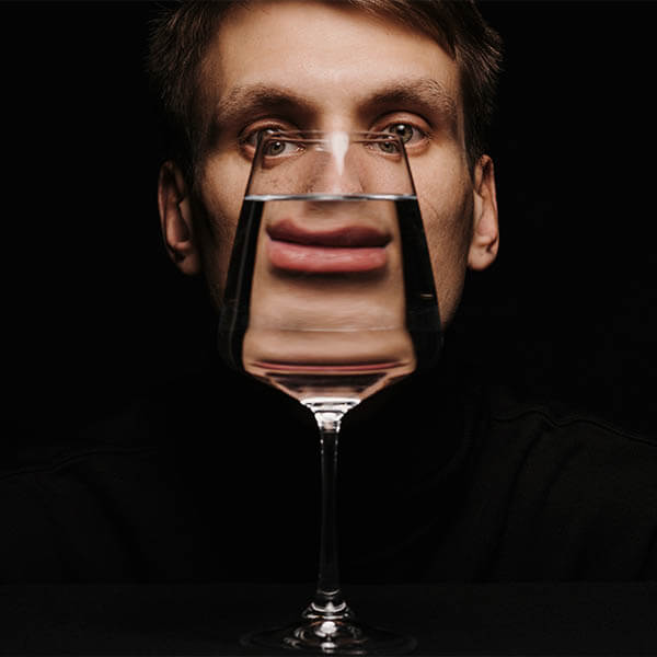 Egy férfi egy pohár vizet tart maga előtt, a folyadék miatt elmosódott az arca.